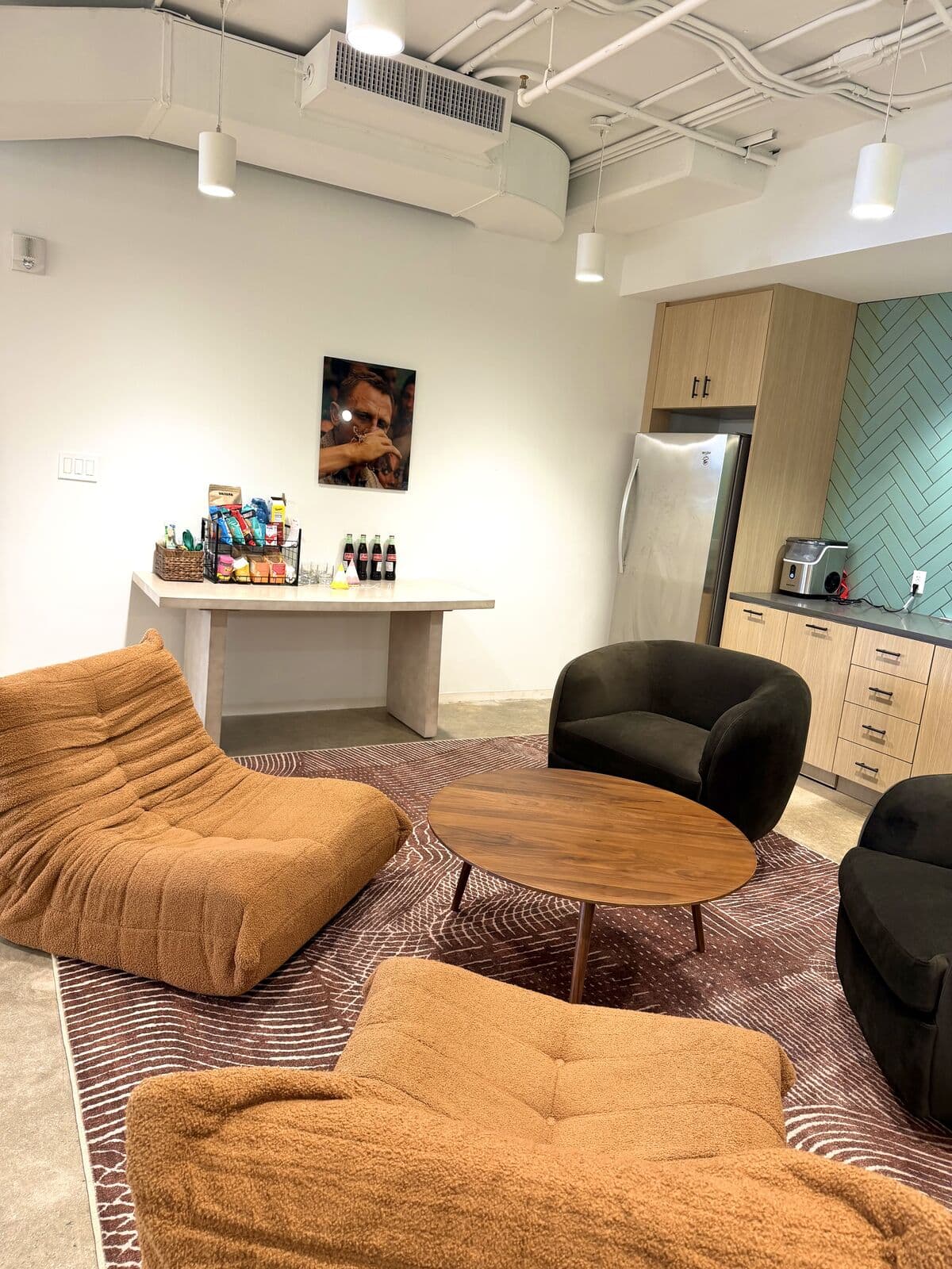 The kitchen after: a rust Togo lounge and black tub chairs around a walnut table beside the stocked snack counter and herringbone tile