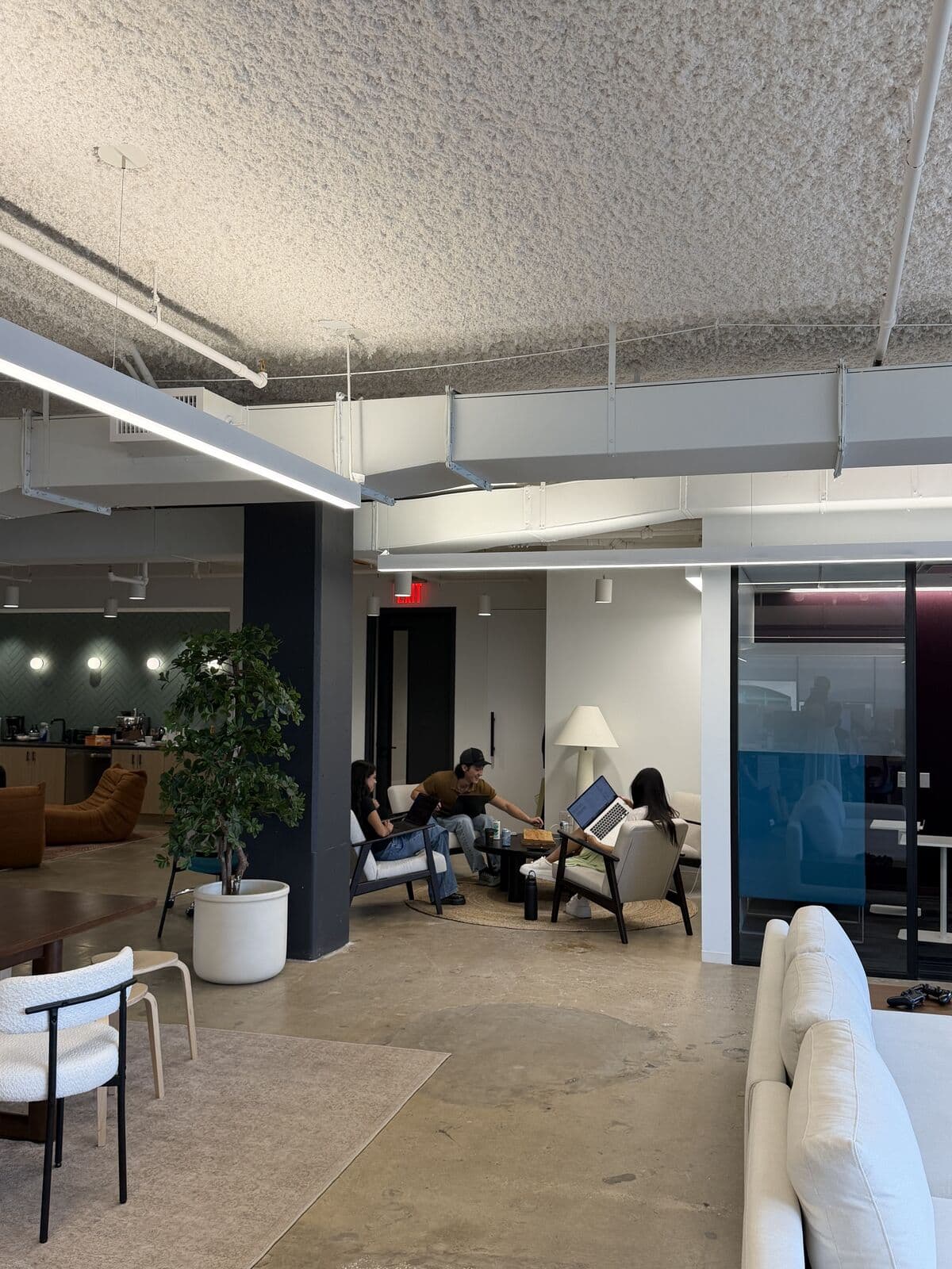 Four zones in one frame: the café, a potted tree, the investor room seating in use, and the living room sectional