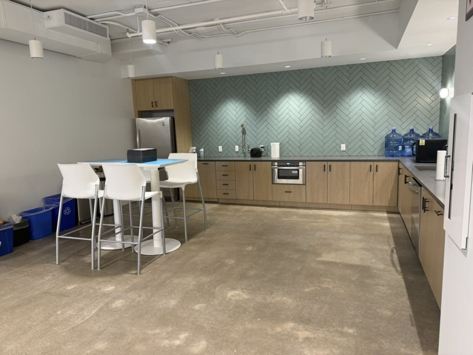 The kitchen before: bare counters, a white high-top table, and recycling bins on unfinished concrete