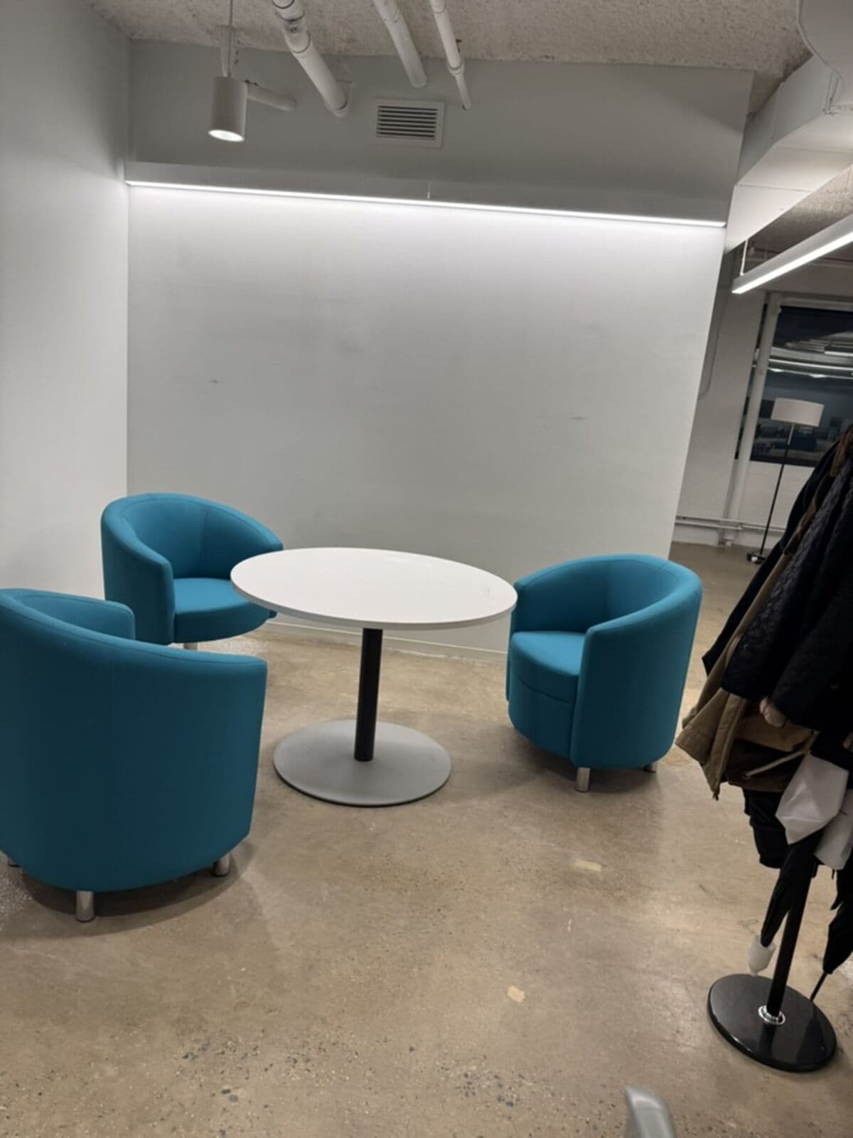 The entrance before: three leftover teal tub chairs around a small white table against a blank wall