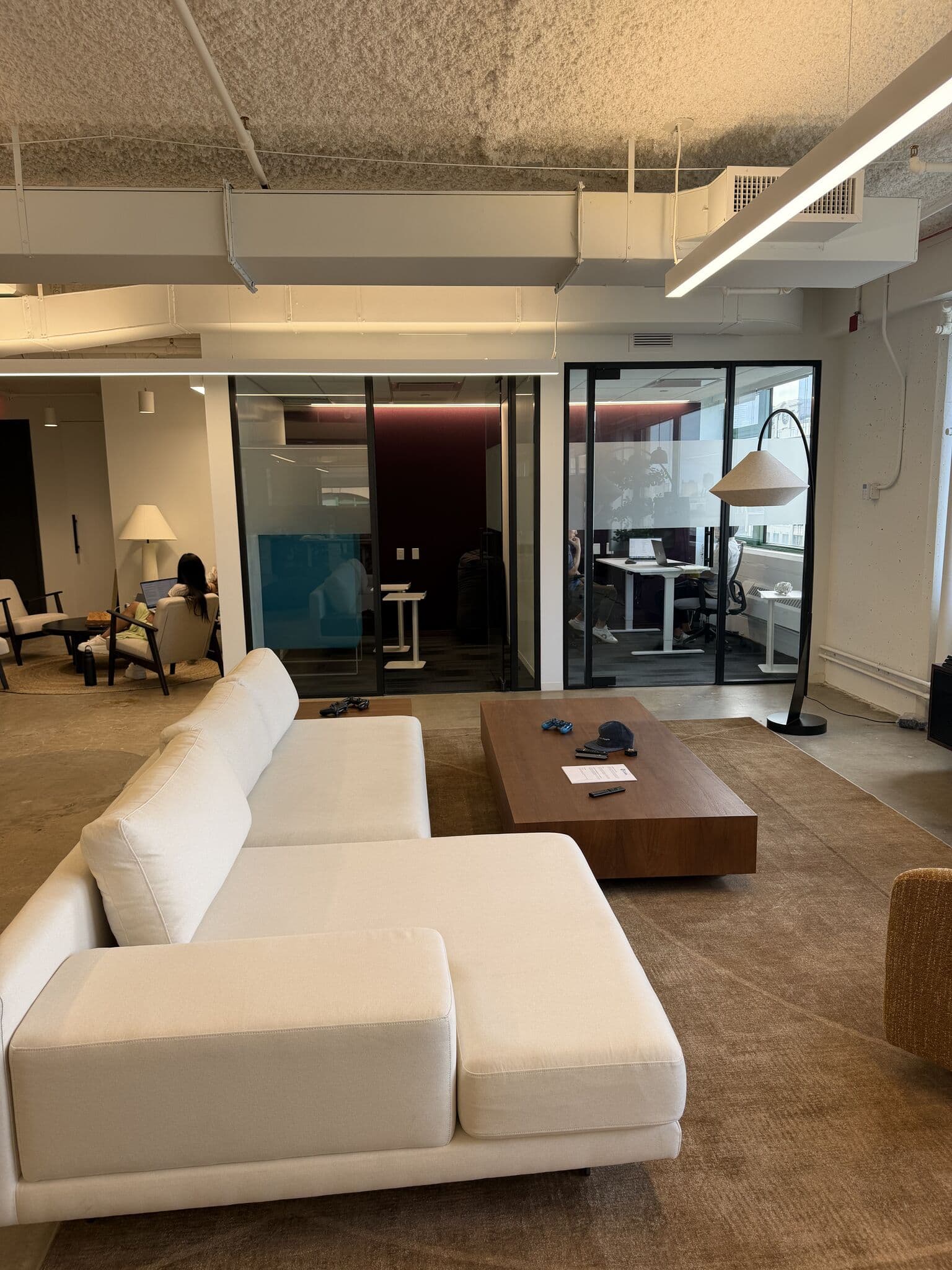 The finished Codes Health living room: a white sectional and walnut coffee table on a warm area rug, with three glass-walled meeting rooms beyond